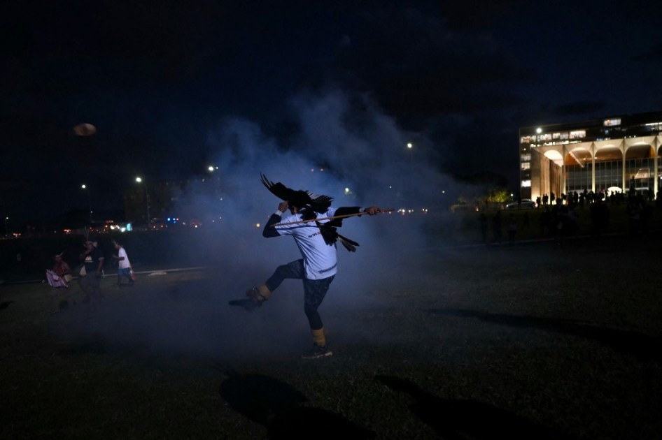 Um indígena brasileiro chuta uma bomba de gás lacrimogêneo ao entrar em confronto com a polícia em frente ao Congresso Nacional, durante a última marcha do Acampamento Terra Livre (ATL), em Brasília,