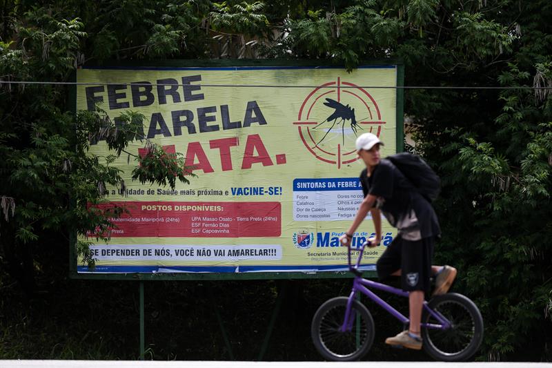 Jovem Passa em frente a cartaz que alerta para os riscos da febre amarela na cidade de Mairiporã
