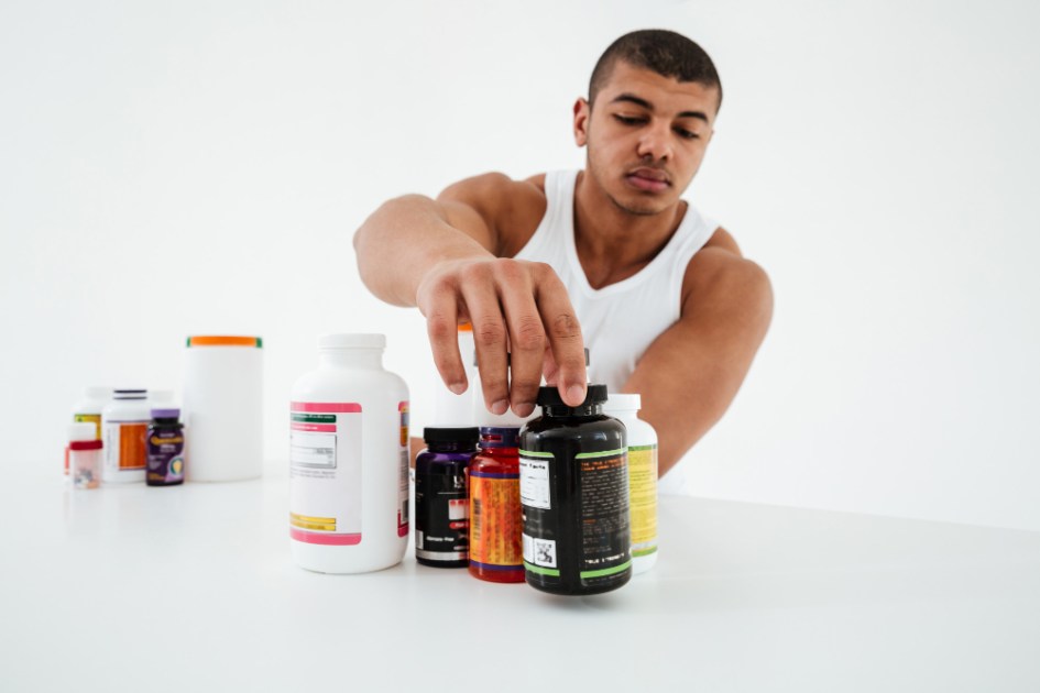 Desportista de pé sobre a parede branca segurando vitaminas