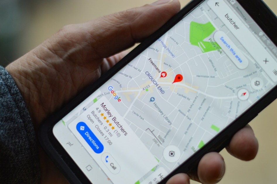 Mão esquerda masculina segurando um celular cuja tela mostra endereço no Google Maps