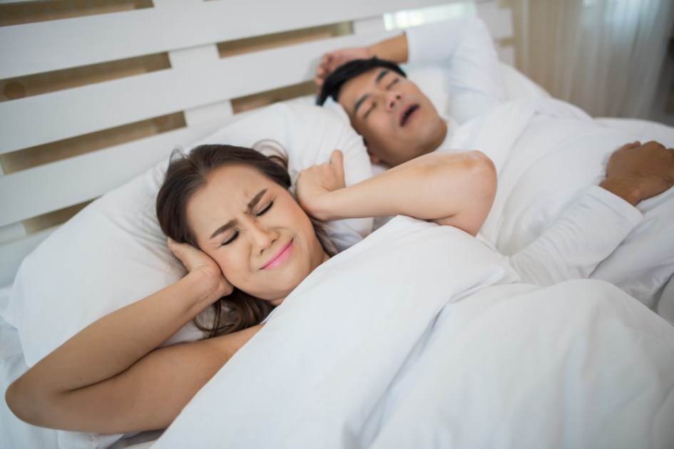 Mulher bloqueando as orelhas com homem dormindo roncando na cama