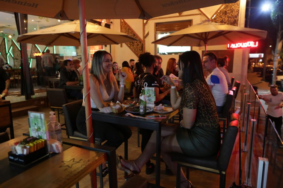 Três mulheres aparecem sentadas na mesa de um bar