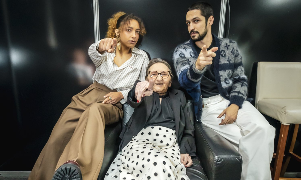 Tânia Maria, Gabriel Leone e Alice Carvalho sentados em poltrona apontando para câmera
