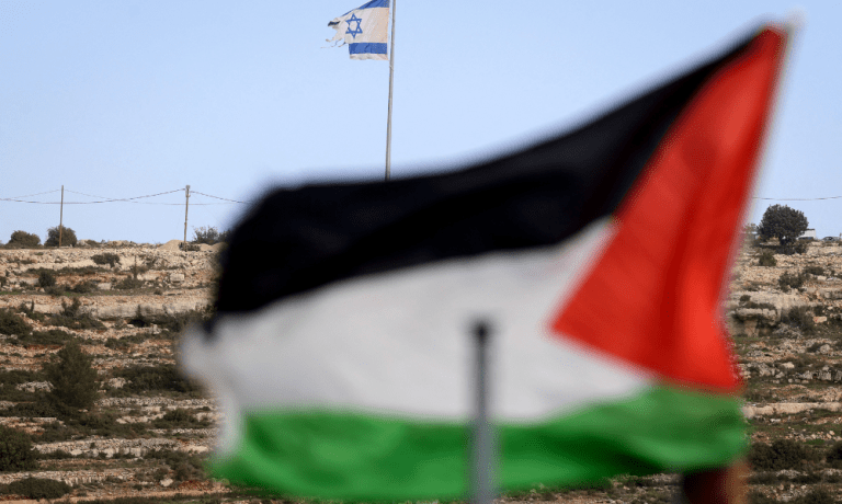 Esta foto, tirada da vila de Umm Safa, ao norte de Ramallah, na Cisjordânia ocupada, mostra uma bandeira palestina (em primeiro plano) e uma bandeira israelense tremulando no topo de uma colina com vista para a vila, em 16 de fevereiro de 2026. O governo de Israel aprovou um processo para registrar terras na Cisjordânia como "propriedade do Estado", atraindo condenação de nações árabes e críticos que disseram que isso aceleraria a anexação do território palestino.