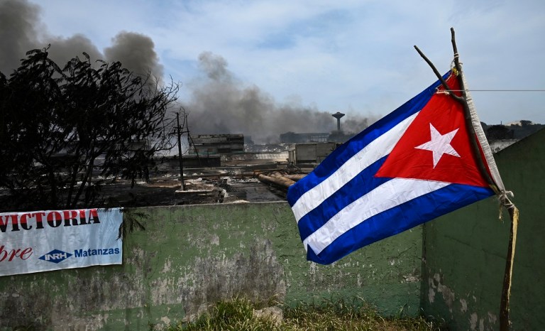 Uma bandeira cubana tremula perto de uma área destruída do depósito de combustível que foi envolvido em chamas por cinco dias depois que um raio atingiu um de seus tanques