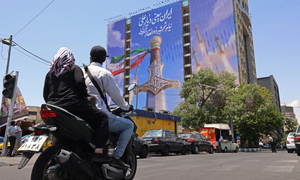 Motoristas passam por uma faixa gigante que retrata mísseis iranianos e uma espada pertencente ao Imã Ali.