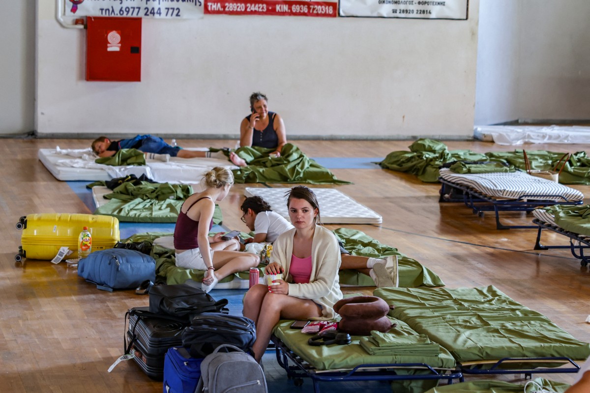 Turistas e moradores locais do vilarejo balneário de Agia Galini se reúnem em um ginásio coberto onde estão temporariamente abrigados durante um incêndio florestal na região de Rethymno, no sudoeste da ilha grega de Creta, em 30 de julho de 2026