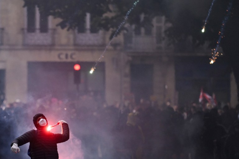 Um manifestante atira um sinalizador de fumaça em direção aos xandarmas franceses durante uma demonstração em protesto contra o "alto custo de vida", em Bordéus, no sudoeste da França, em 17 de outubro de 2026, como parte de uma convocação nacional de mobilização que reúne vários grupos expressando sua indignação: ex-integrantes dos "Coletes Amarelos", estudantes do ensino médio e universitários, ativistas climáticos e até mesmo agricultores.